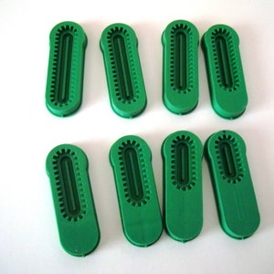 May include: Eight green plastic pieces with a raised design. The pieces are shaped like a long oval with a groove down the center.