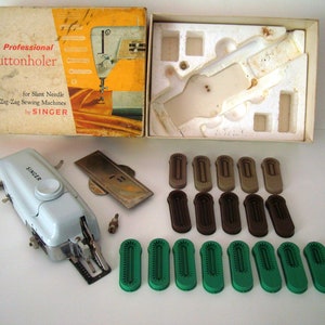 May include: A white Singer buttonholer attachment for zig zag sewing machines. The attachment is in its original box with various sized plastic buttonhole feet.