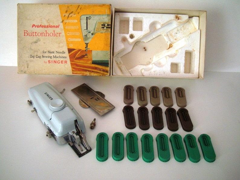 May include: A white Singer buttonholer attachment for zig zag sewing machines. The attachment is in its original box with various sized plastic buttonhole feet.