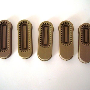 May include: Five brown plastic zipper pulls with a textured design. Each pull has a rectangular opening in the center.