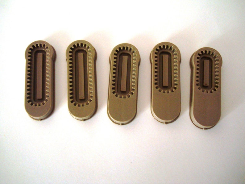 May include: Five brown plastic zipper pulls with a textured design. Each pull has a rectangular opening in the center.