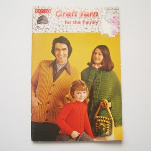 Könnte beinhalten: Ein Vintage-Heft von Patons Craft Yarn for the Family mit einer dreiköpfigen Familie, die gestrickte Kleidung trägt. Das Cover zeigt einen gelben Hintergrund mit einer dreiköpfigen Familie, einem Mann, einer Frau und einem Kind, die alle gestrickte Kleidung tragen. Der Mann trägt einen braunen Cardigan, die Frau einen grünen Schal und das Kind einen roten Pullover.