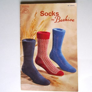 Może przedstawiać: Wzornik do robienia na drutach vintage dla skarpet zatytułowany "Socks by Beehive". Okładka przedstawia trzy pary skarpet w kolorze niebieskim, czerwonym i białym.