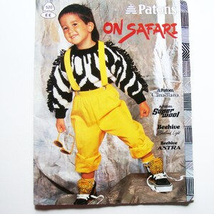 Peut inclure: Une couverture de magazine vintage avec un enfant portant un pull zébré, un pantalon jaune avec des bretelles et des baskets montantes à motifs. Le texte "ON SAFARI" est affiché en haut. Le magazine présente également les logos Patons et Super Wool.