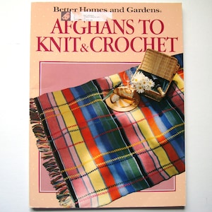 Könnte beinhalten: Ein Buchcover mit dem Titel "Afghans to Knit & Crochet" von Better Homes and Gardens. Das Cover zeigt eine bunte gestreifte gehäkelte Decke mit einem Picknickkorb und Blumen.