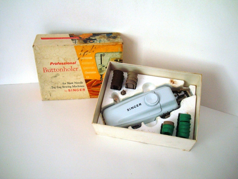 May include: A white Singer brand buttonholer in its original box. The box is white with red and yellow text that reads "Professional Buttonholer for Slant Needle Zig Zag Sewing Machines by SINGER".