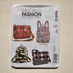 May include: A McCall's Fashion Accessories sewing pattern. The image shows illustrations of four bag designs: a floral shoulder bag, a patterned backpack, a camouflage backpack, and a pink and black plaid bag. The pattern number is M6410.