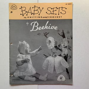 May include: A vintage knitting and crochet pattern book for baby sets by Beehive. The cover features a black and white photo of a baby wearing a crocheted outfit and a hat. The book is titled "Baby Sets in Knitting and Crochet by Beehive" and is priced at 40 pence.