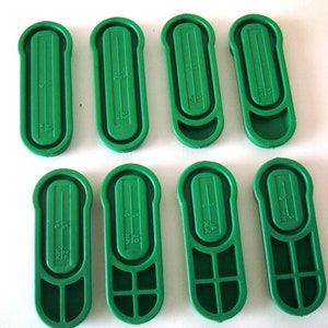 May include: Eight green plastic measuring scoops with different measurements marked on them. The measurements are in milliliters (ml).