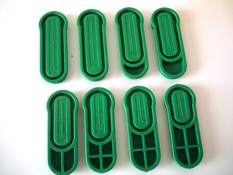 May include: Eight green plastic measuring scoops with different measurements marked on them. The measurements are in milliliters (ml).