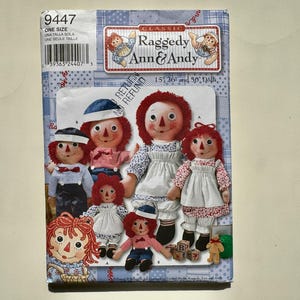 May include: A sewing pattern for Raggedy Ann & Andy dolls. The pattern cover features illustrations of the dolls in various sizes, with red yarn hair, and wearing dresses and sailor outfits. The cover has a blue and white patchwork design.