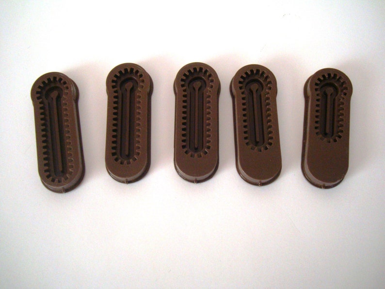 May include: Five brown plastic zipper pulls with a textured design. The zipper pulls have a small hole in the center.