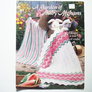 Könnte beinhalten: Ein Buch mit dem Titel "A Garden of Baby Afghans" von Sandy Scoville, das eine weiße gehäkelte Babydecke mit rosa und grünen Streifen und einen Korb mit Wassermelonen zeigt.