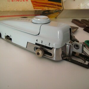 May include: A white Singer brand sewing machine with a silver base and a black foot pedal. The machine has a dial with numbers 1, 2, 3, and 4.