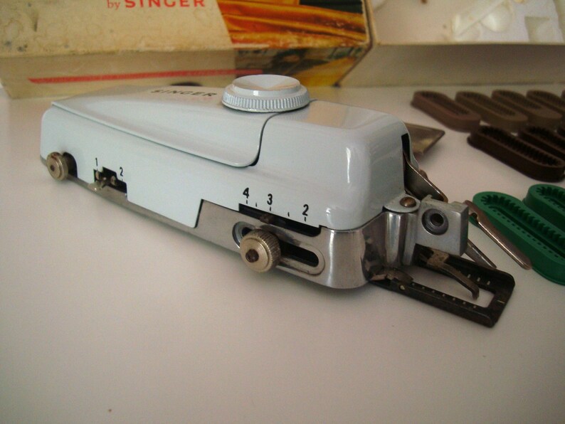 May include: A white Singer brand sewing machine with a silver base and a black foot pedal. The machine has a dial with numbers 1, 2, 3, and 4.