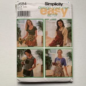 May include: A sewing pattern booklet with the title "Simplicity design your own easy apron" and four images of women wearing different aprons. The aprons are in various colours and patterns, including floral, polka dot, and striped.