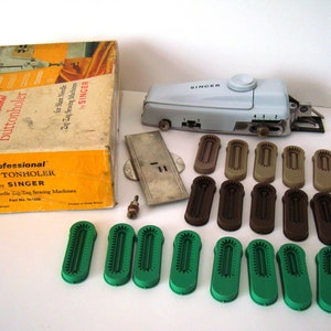 May include: A white Singer brand professional buttonholer with a box, a metal plate, and various sized plastic buttonhole attachments in green, brown, and beige.