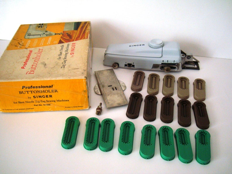 May include: A white Singer brand professional buttonholer with a box, a metal plate, and various sized plastic buttonhole attachments in green, brown, and beige.