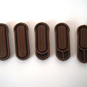 May include: Five brown plastic curtain tiebacks with a textured surface and a small hole at the top. Each tieback has a different measurement printed on it.
