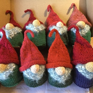 May include: Eight knitted gnome ornaments with red, green and blue hats. The gnomes have white beards and yellow noses.