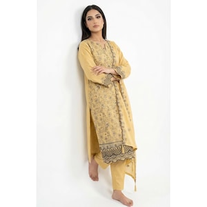 May include: A woman wearing a mustard yellow embroidered kurta suit. The long-sleeved tunic and matching pants feature intricate floral patterns and decorative borders. The outfit is made of a lightweight fabric.