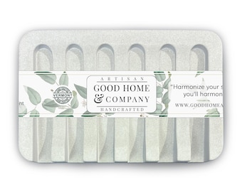 May include: A rectangular, light gray soap dish with a textured surface. The dish has a series of vertical ridges and arched cutouts. A white label with green leaf accents and the text "GOOD HOME & COMPANY" is across the front.