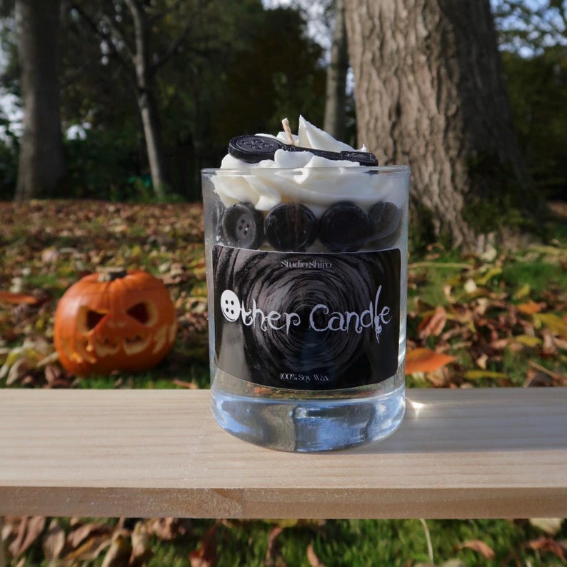 May include: A black and white candle with a black and white button design. The candle is in a clear glass jar with a black label that says "Other Candle" and "100% Soy Wax".