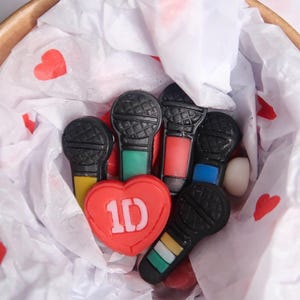 May include: A red heart-shaped charm with the text "1D" inside, surrounded by black and white microphone charms in a white tissue-lined container.