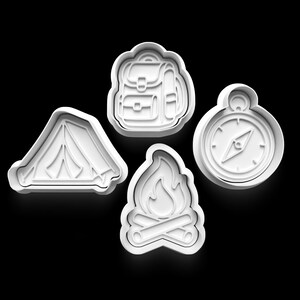 Op de afbeelding: Vier witte cookie cutters met een campingthema. De set bevat een tent, rugzak, kampvuur en kompas. De vormen zijn omlijnd met een verhoogde rand, perfect voor het maken van gedetailleerde koekjes.