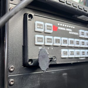 May include: Close-up of a black control panel with white buttons and a black knob. The buttons are labeled with text such as "WARN", "STBY", and "RADIO". The text "FEDERAL SIGNAL PATHFINDER" is also visible.