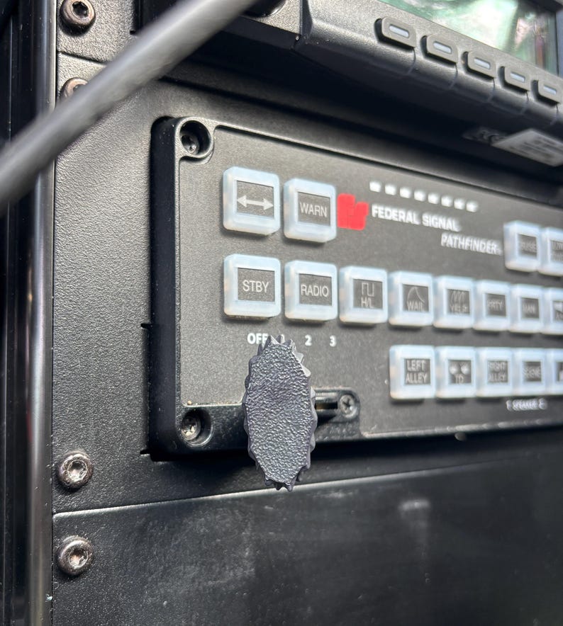 May include: Close-up of a black control panel with white buttons and a black knob. The buttons are labeled with text such as "WARN", "STBY", and "RADIO". The text "FEDERAL SIGNAL PATHFINDER" is also visible.