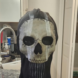May include: A skull mask with a distressed, aged appearance. The mask features a skull design with large eye sockets and a prominent nose cavity. Vertical white stripes accent the forehead and chin. The mask is attached to a black hood.
