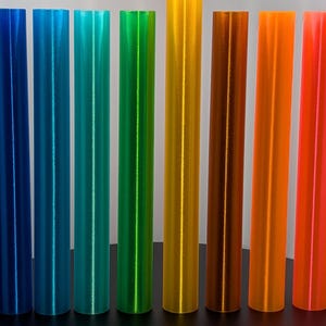 May include: A set of ten colorful, cylindrical tubes with a shiny, metallic finish. The tubes are arranged in a row from left to right, with the colors transitioning from purple to red.