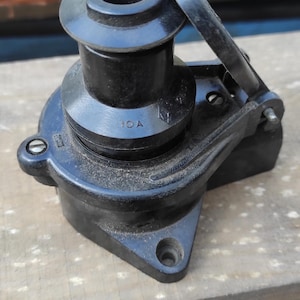 May include: A black electrical socket with a hinged protective cover, featuring a cylindrical center and a mounting base with screw holes. The component is marked with the text 10A, indicating its electrical current rating capacity.