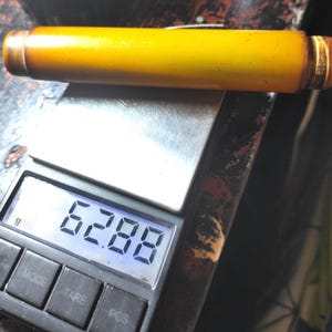 May include: A yellow cylindrical object with brown ends rests on a digital scale. The scale displays a weight of 62.88 grams. The object appears to be made of wood or a similar material.