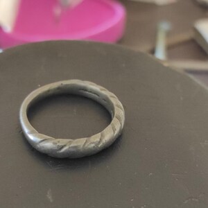 May include: A silver-toned metal ring featuring a continuous twisted or rope-like texture around the entire band. The surface of the ring appears matte and shows signs of wear, with a consistent circular shape and a uniform thickness throughout.