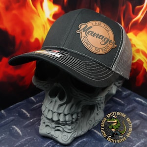 May include: A black and gray trucker hat with a brown leather patch that says "I am the Manager Karen So Fafo".