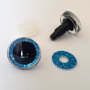 Puede incluir: Un juego de ojos para manualidades con una c&uacute;pula de pl&aacute;stico transparente, pupila negra e iris de purpurina azul brillante. El juego incluye un ojo montado con un poste de pl&aacute;stico negro, una arandela de purpurina azul y una arandela de fijaci&oacute;n.