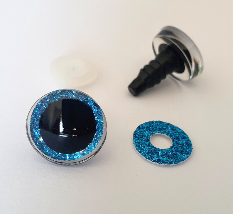 Puede incluir: Un juego de ojos para manualidades con una c&uacute;pula de pl&aacute;stico transparente, pupila negra e iris de purpurina azul brillante. El juego incluye un ojo montado con un poste de pl&aacute;stico negro, una arandela de purpurina azul y una arandela de fijaci&oacute;n.