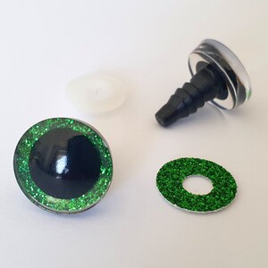Puede incluir: Un juego de ojos para manualidades con pupila negra rodeada por un iris de purpurina verde brillante. El conjunto incluye un ojo ensamblado con un poste de pl&aacute;stico negro, una arandela de pl&aacute;stico transl&uacute;cido y un anillo de purpurina verde.