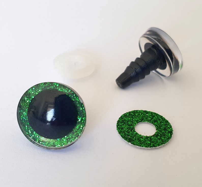 Puede incluir: Un juego de ojos para manualidades con pupila negra rodeada por un iris de purpurina verde brillante. El conjunto incluye un ojo ensamblado con un poste de pl&aacute;stico negro, una arandela de pl&aacute;stico transl&uacute;cido y un anillo de purpurina verde.
