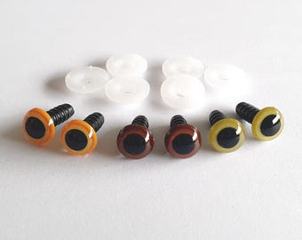 May include: A selection of craft safety eyes in various colours, including orange, brown, and yellow, each with a black pupil. White plastic washers are also present. These eyes are suitable for making soft toys and other craft projects.