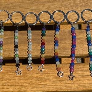 May include: Twelve beaded keychains with silver key rings and charms. The charms are either a star or a heart. The beads are various colors, including black, purple, green, blue, red, and white.