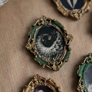Könnte beinhalten: Miniatur-Zierrahmen im Vintage-Stil mit goldenen und grünen Akzenten. Jeder Rahmen enthält ein kleines Porträt, darunter eine schwarze Katze mit Rüschenkragen und andere antike Bilder. Dekorativ und einzigartig.