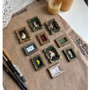 May include: Ten miniature gold frames with green velvet mats, each containing a different image. The frames are arranged in a random pattern on a brown paper surface.