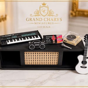 May include: A 1:12 scale miniature set featuring a black DX7 synthesiser, a black boombox, a record player, a silver microphone, a music album titled Greatest Hits of all time, and a white acoustic guitar, all displayed on a black shelf unit.