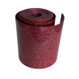 May include: A roll of burgundy glitter vinyl. The vinyl is rolled up, revealing the inner layers. The surface is covered in small, sparkling glitter particles, giving it a textured appearance. The edges are smooth and slightly curved.