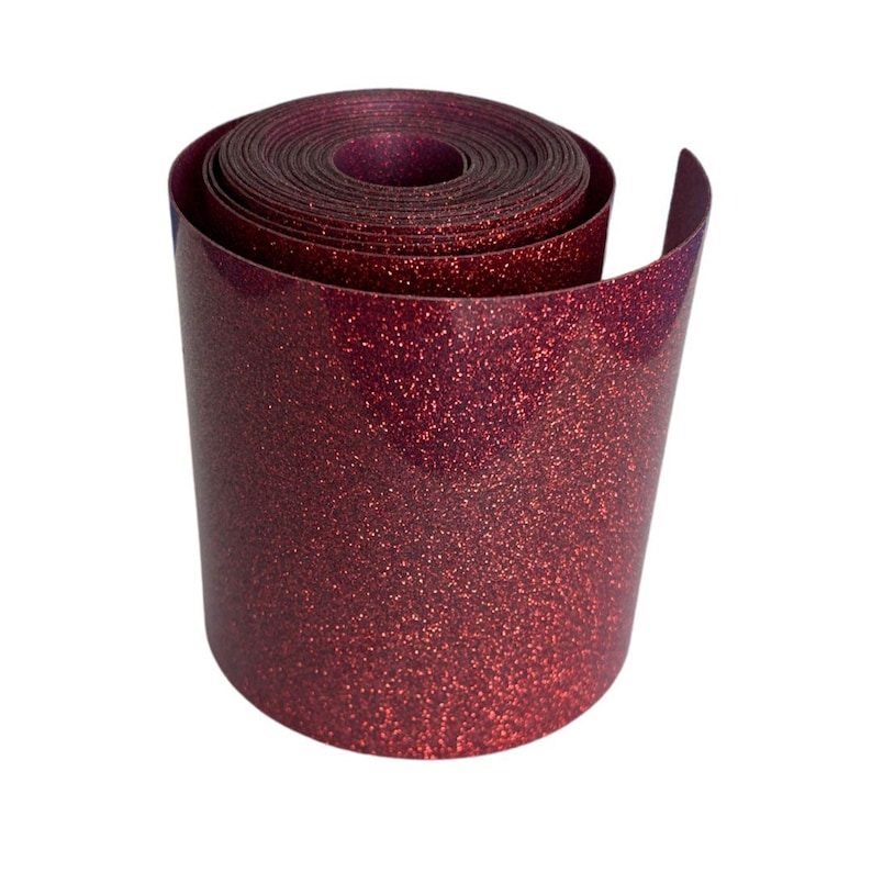 May include: A roll of burgundy glitter vinyl. The vinyl is rolled up, revealing the inner layers. The surface is covered in small, sparkling glitter particles, giving it a textured appearance. The edges are smooth and slightly curved.