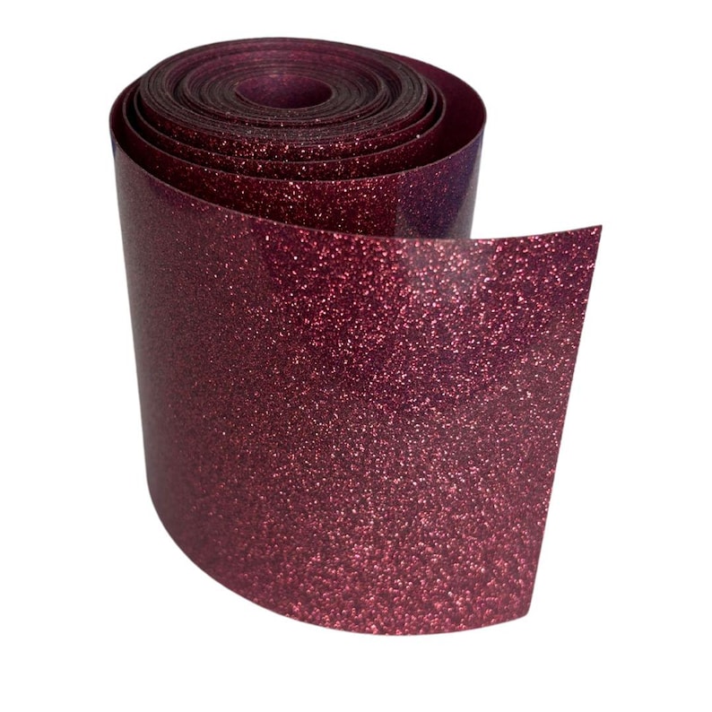 May include: A roll of burgundy glitter vinyl. The vinyl is rolled up, with the end unfurled, revealing the shiny, textured surface. The glitter is evenly distributed across the material, catching the light and creating a sparkling effect. The roll is set against a white background.