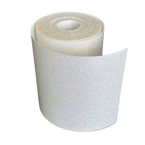 May include: A roll of white glitter tape, unrolled to reveal the sparkly texture. The tape is a bright white with iridescent glitter, creating a shimmering effect. The roll is tightly wound, showing the layers of tape.